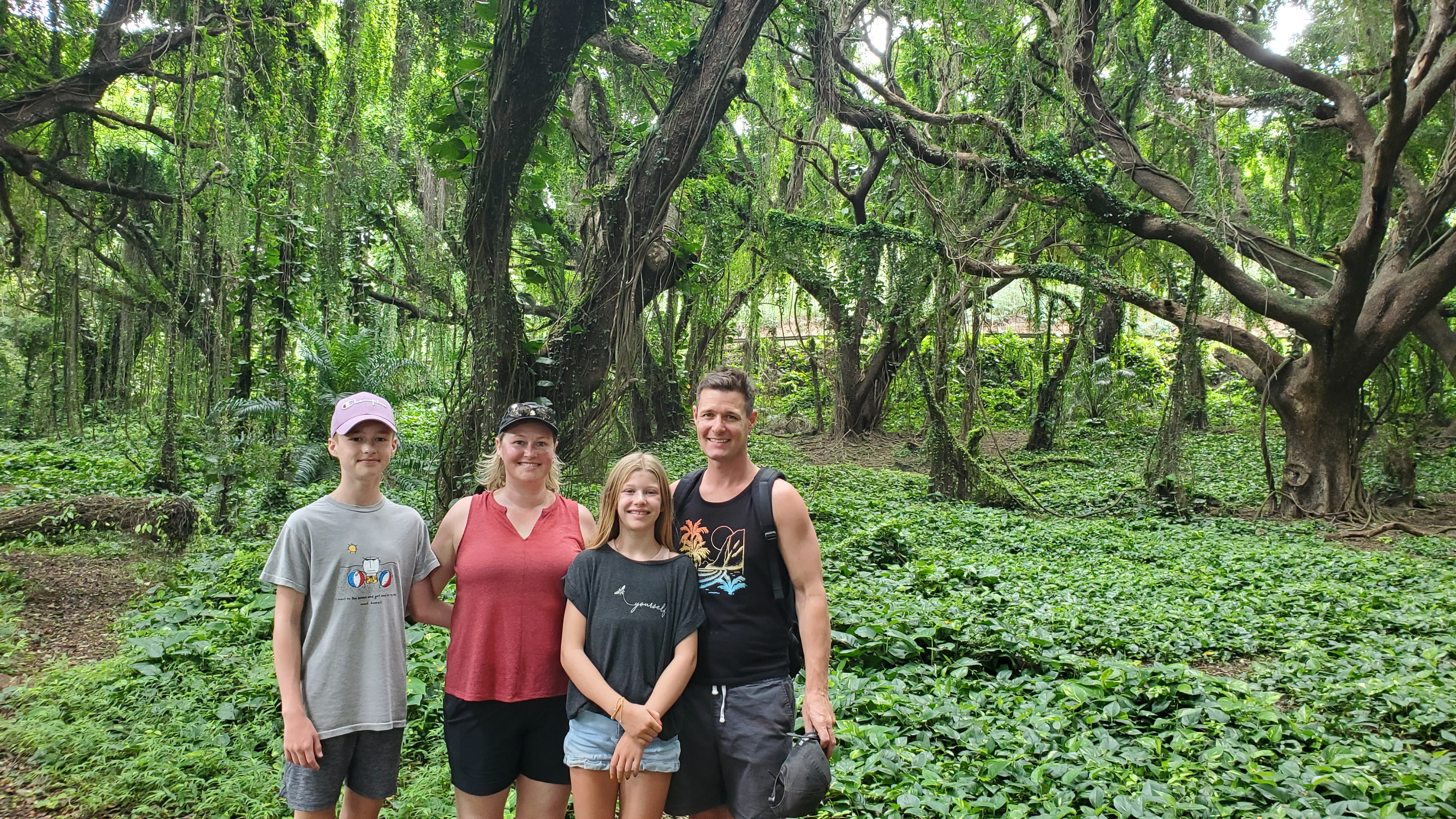 Man, woman and teenagers, family of mother, father, son, daughter, standing in lush green forest with trees and foliage