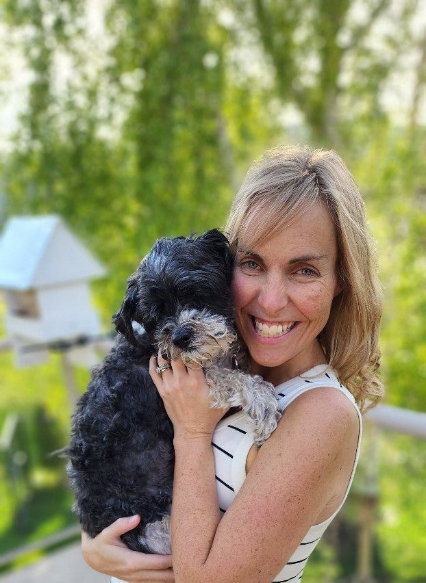 A woman poses for a picture with her small, fluffy dog that has black and white fur.