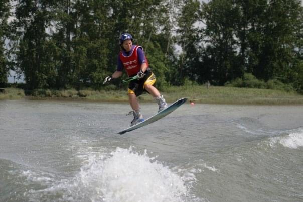 Woman wearing safety gear lifting off the water on a wakeboard.