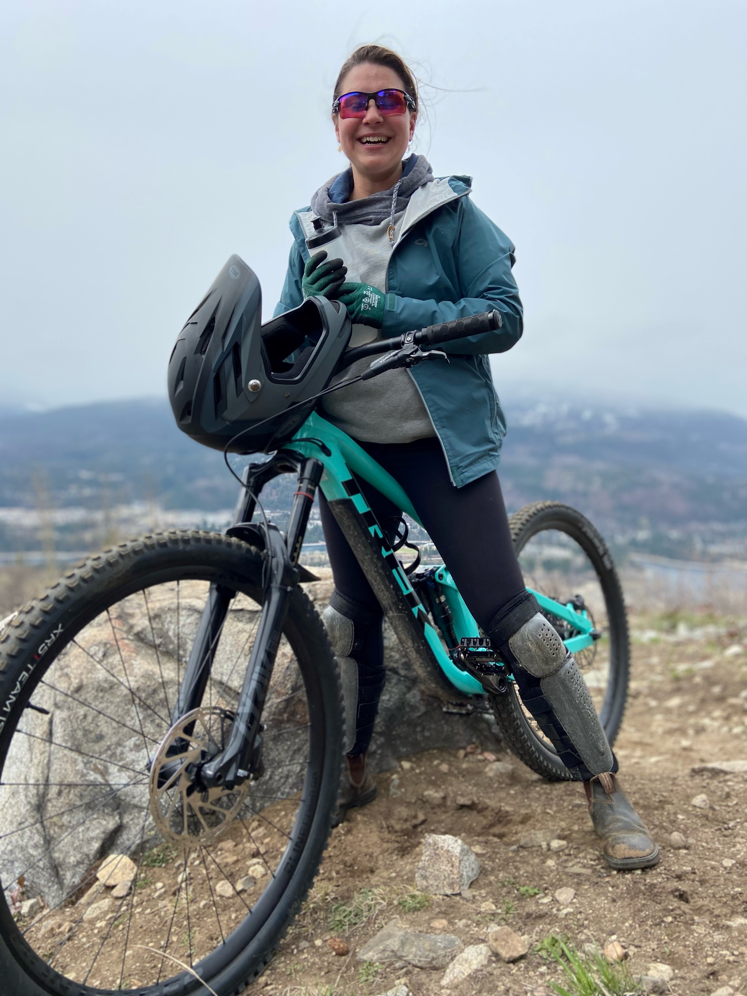 A woman in cycling gear sitting on a bike, with mountains in the background.