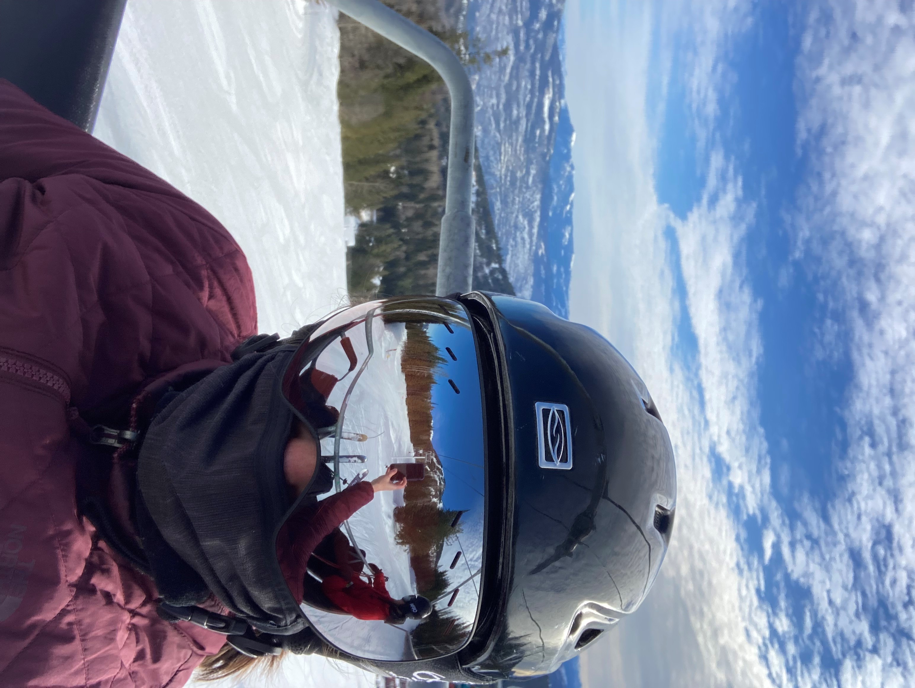 A person in skiing gear takes a selfie while on a chair lift.