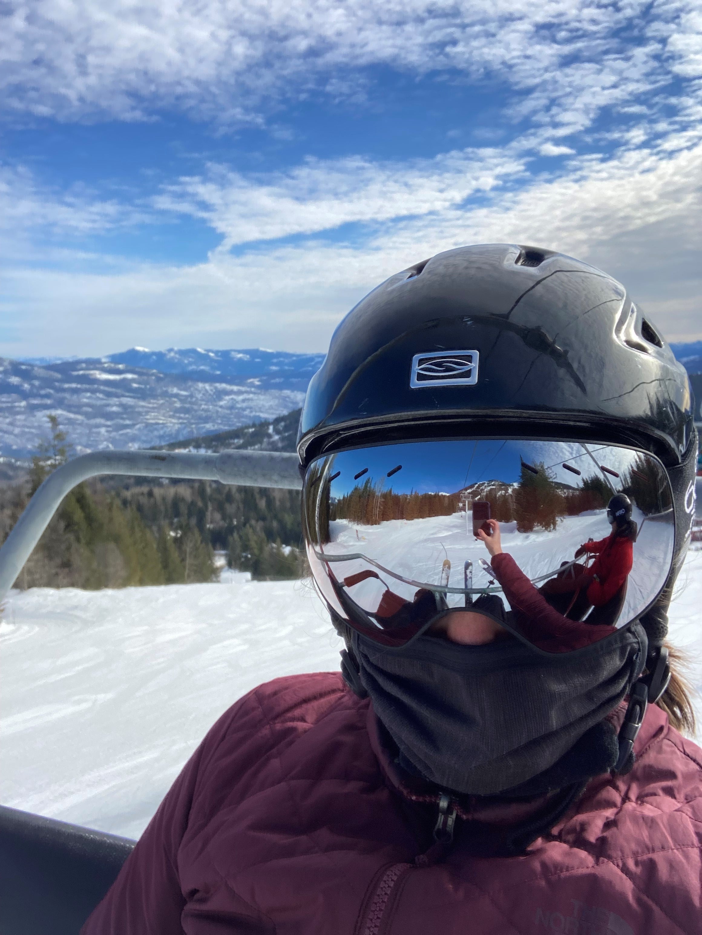 A person in skiing gear takes a selfie while on a chair lift.