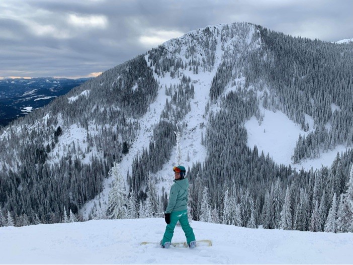 A woman on a snowboard in a helmet in front of a snowy mountain peak