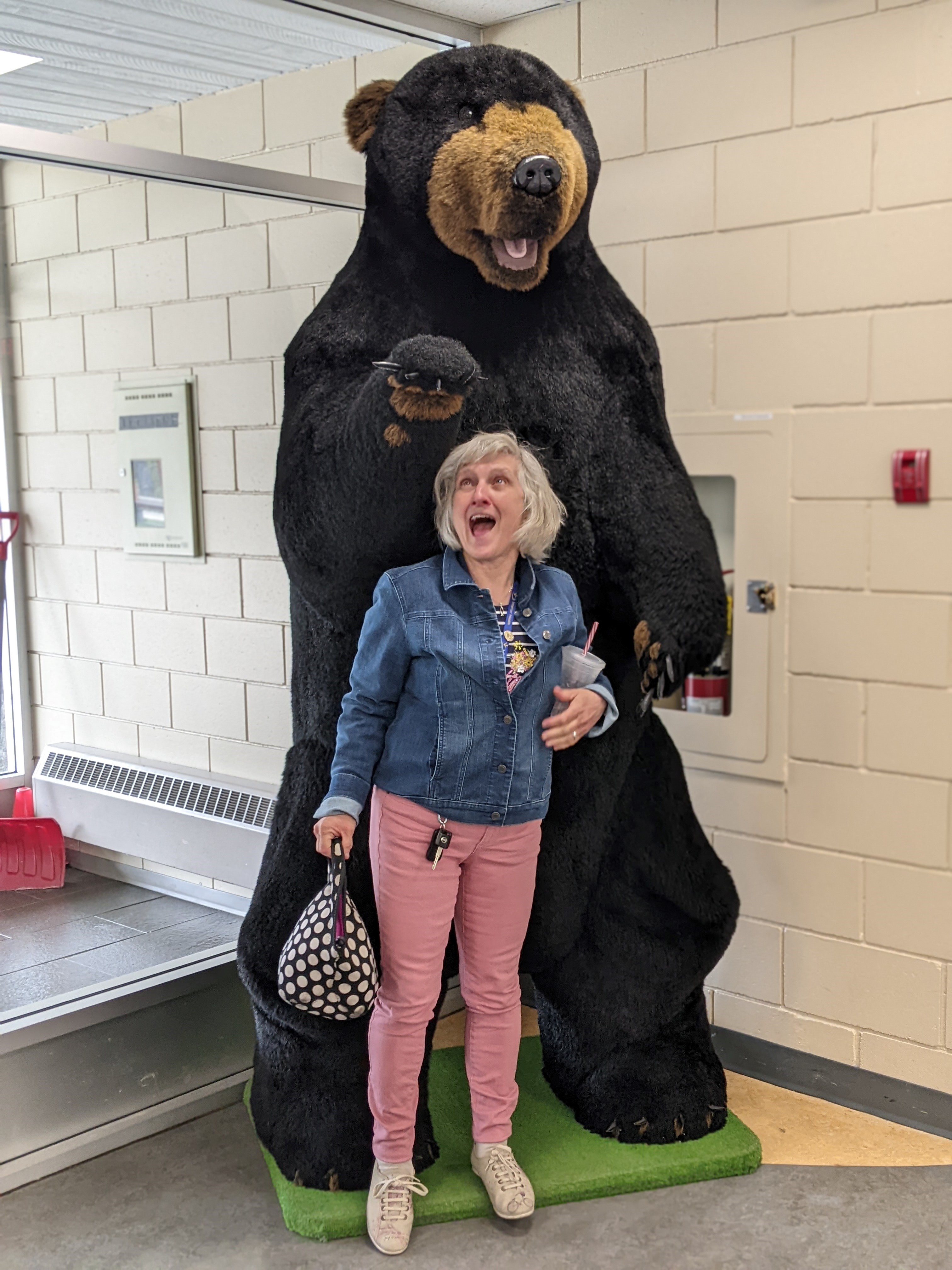 A woman pretending to look scared in front of a large, stuffed bear.