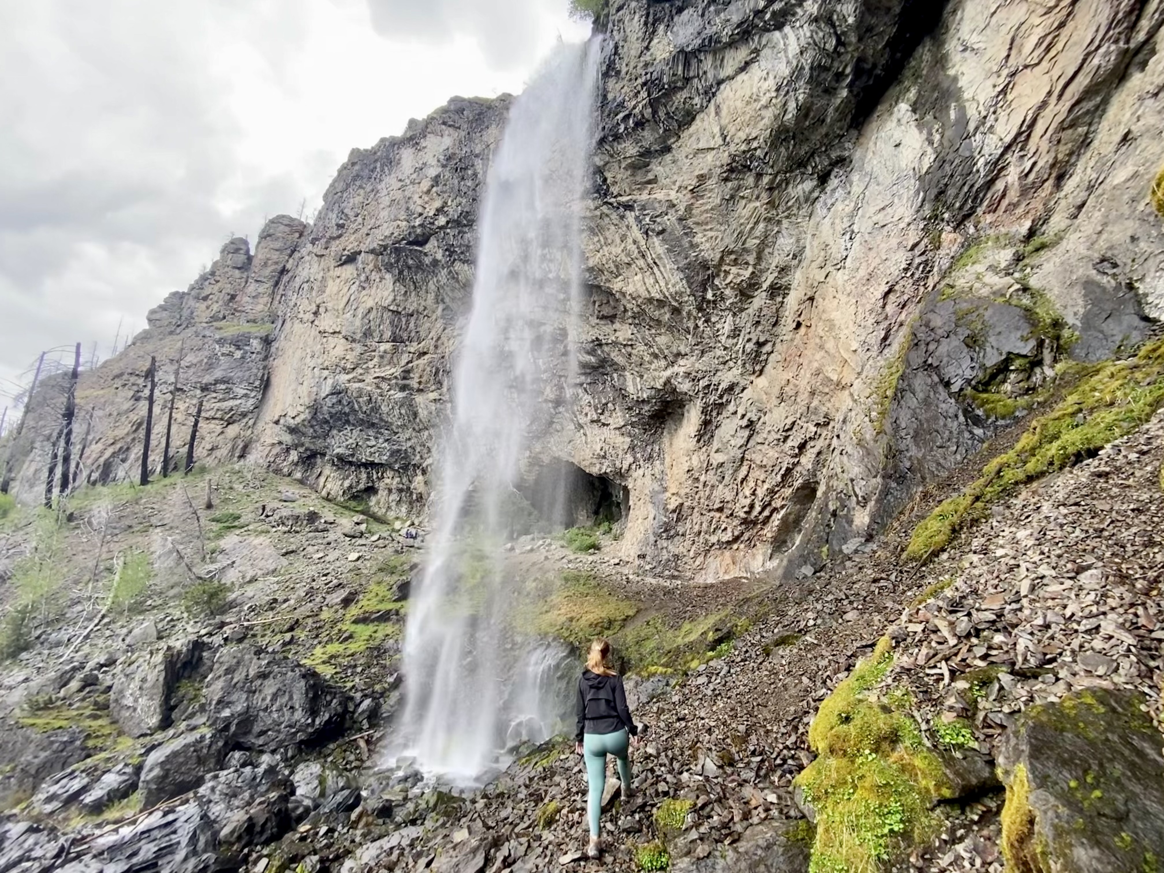 Woman hiking up a mountain next to a waterfall