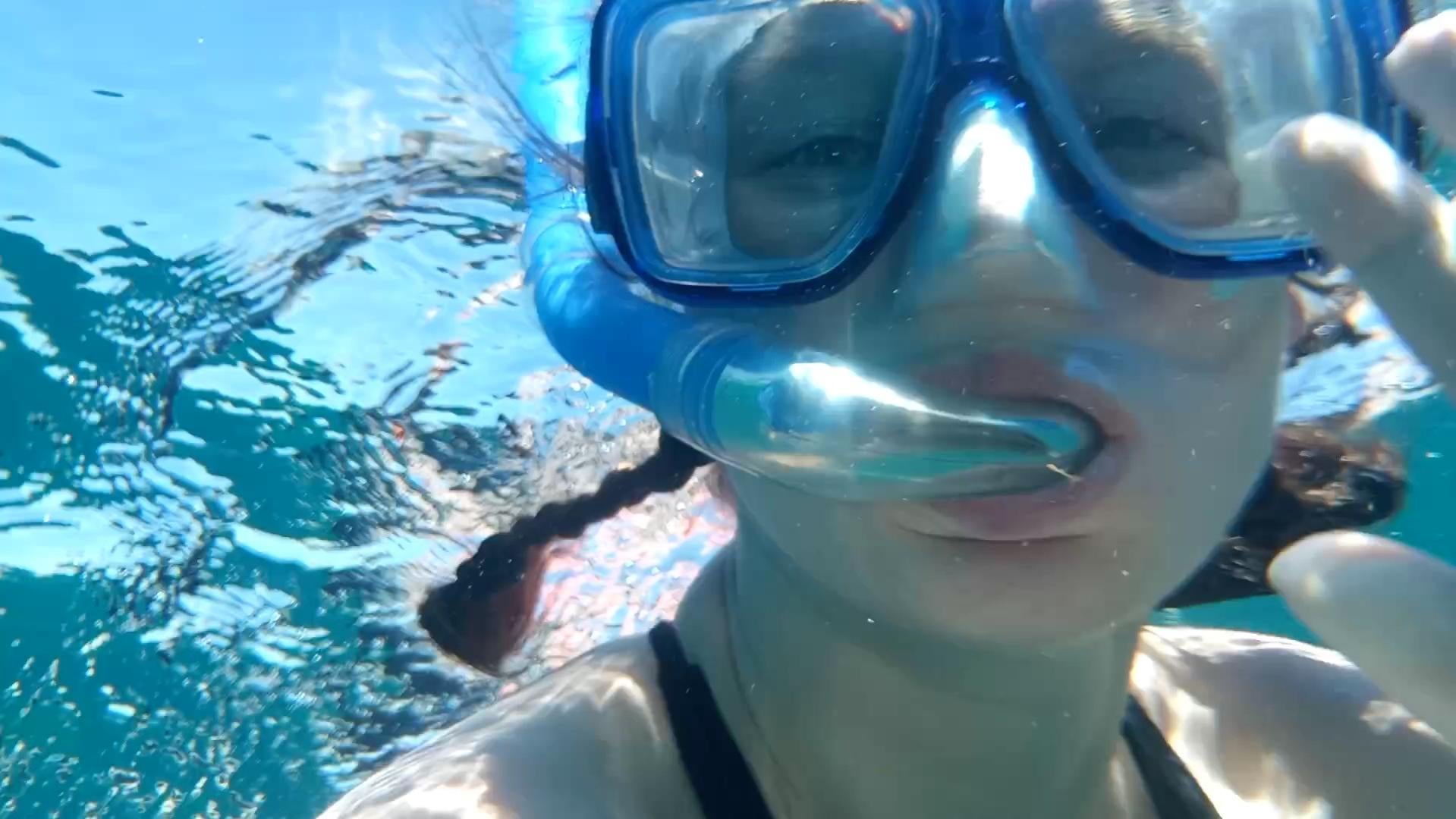 Underwater woman with braided brown hair snorkelling and wearing goggles.