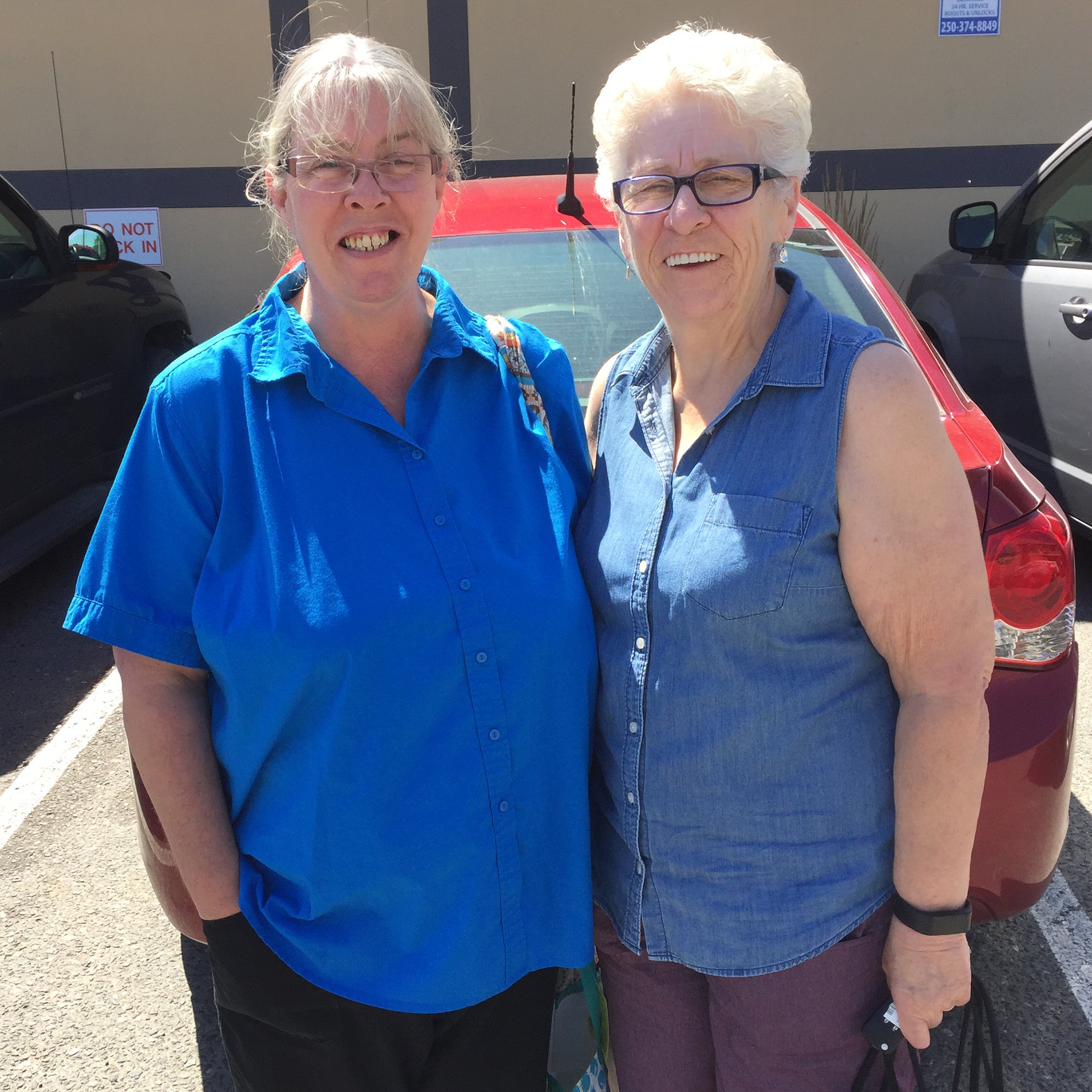 two women wearing glasses standing side by side and smiling to camera