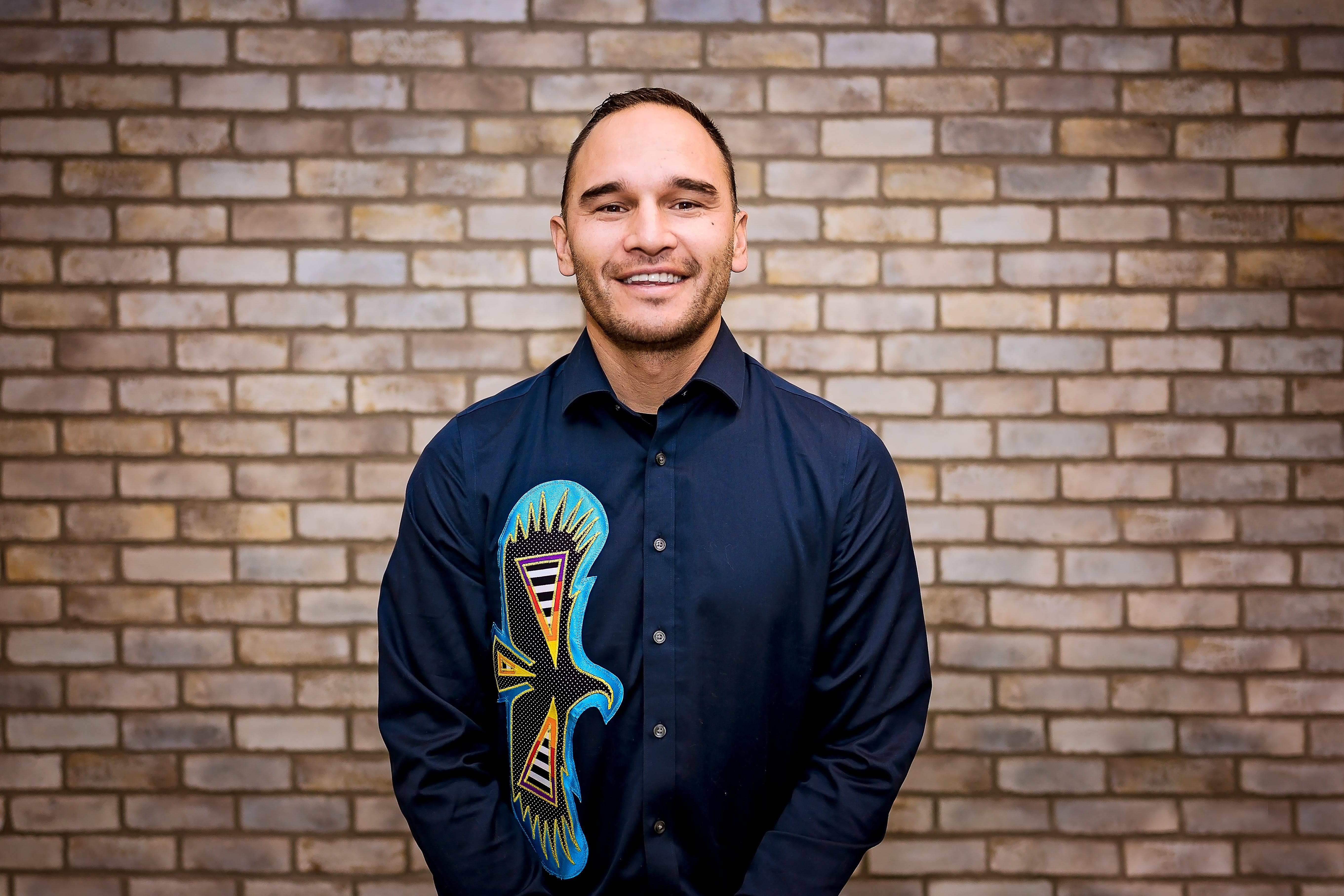 Person wearing blue long sleeve with an Indigenous eagle design, smiling