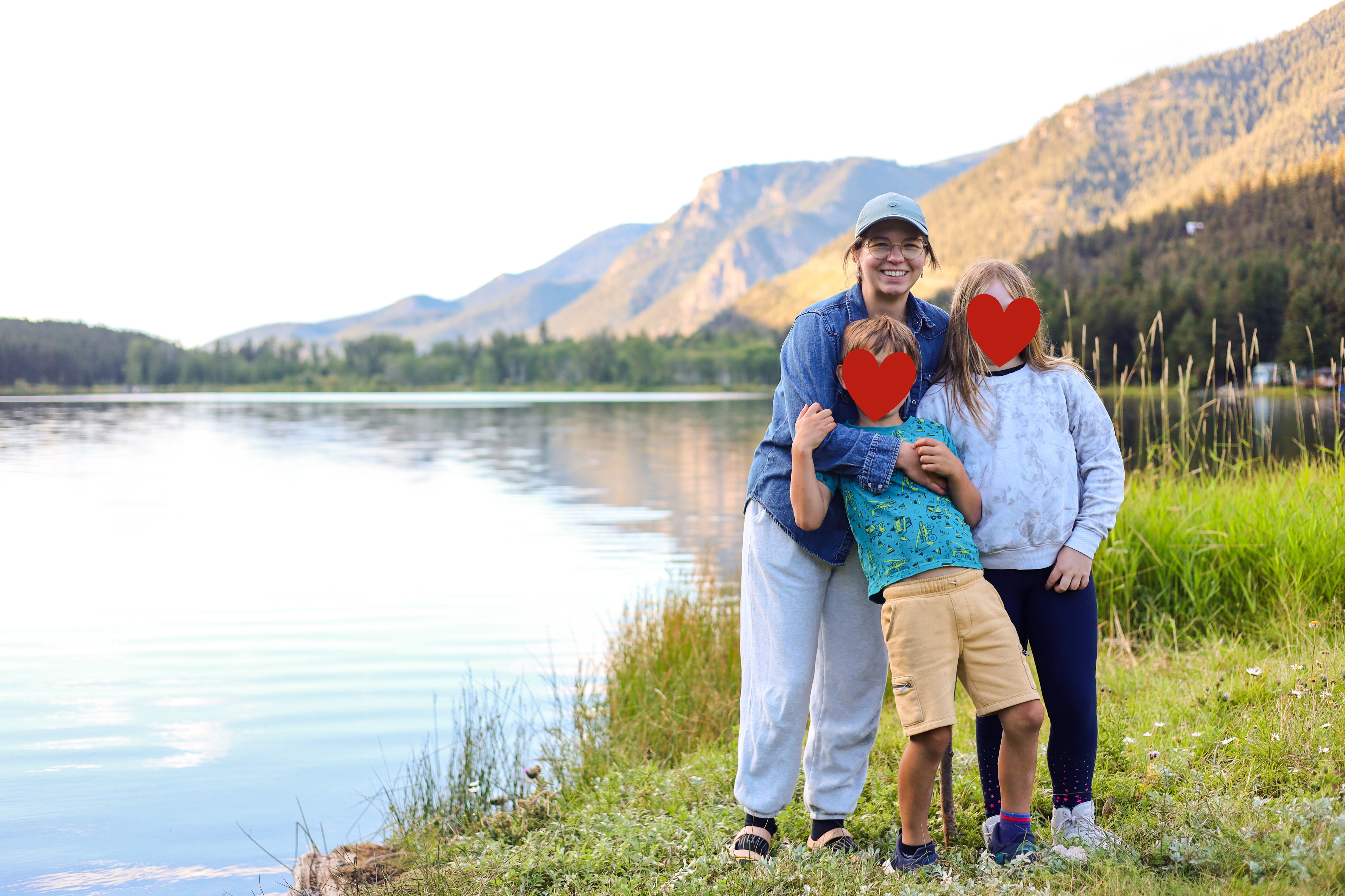 A woman standing beside two children in front of a mountain lake.