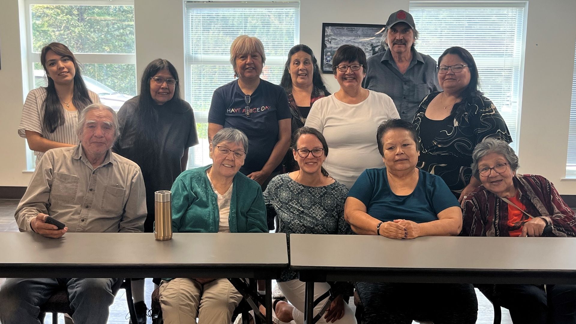 A group of Elders sitting and standing behind a table, smiling, with Nancy sitting in the centre. 