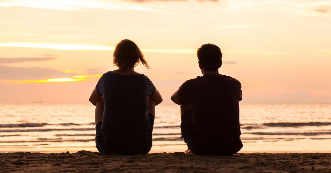 Two youth sit on the beach looking out at the water.