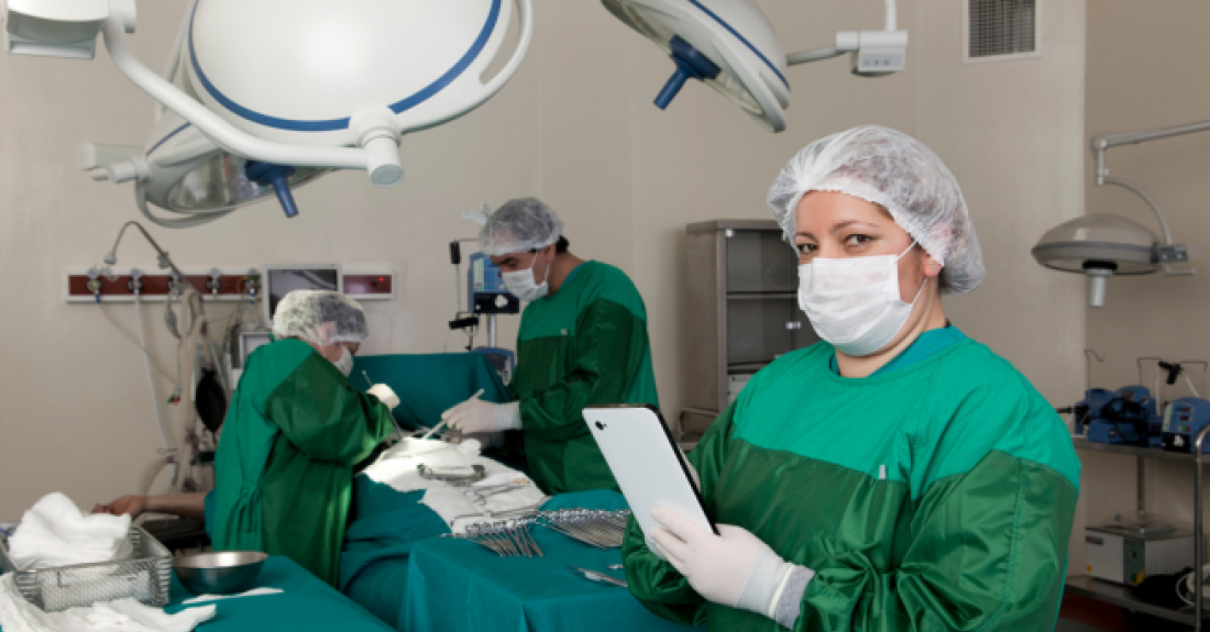 Two people performing dental surgery in the background, one person in the foreground wearing a mask and holding a clipboard. 