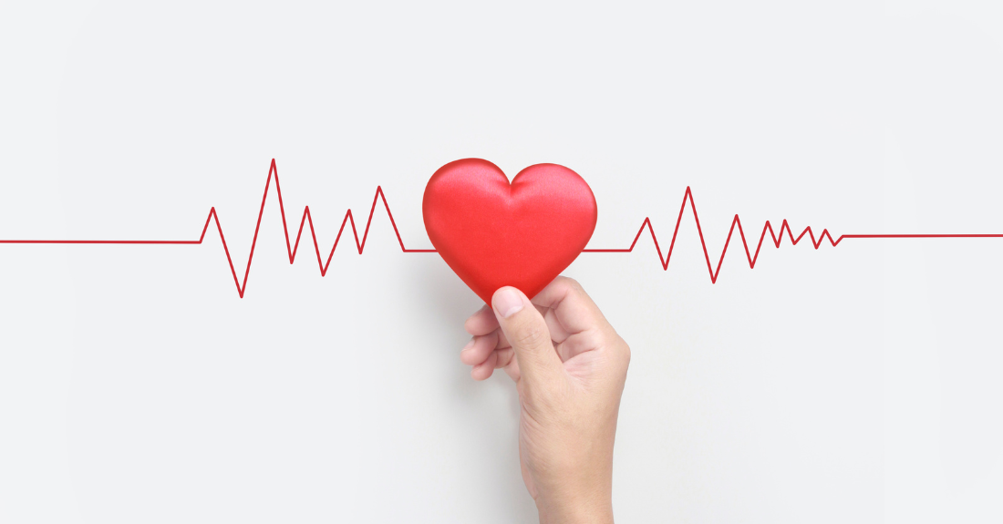 A hand holds up a fake red heart in the middle of a point where two red wavy lines meet.