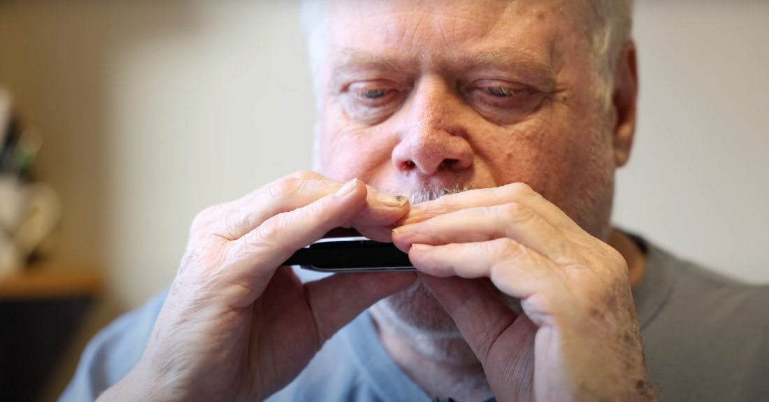An up close picture of an older person with grey hair playing a harmonica.