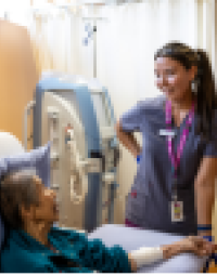 A nurse tends to a patient who is sitting up in a hospital bed.