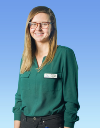 A profile shot of a woman with dark blonde hair wearing a green shirt with a name tag (reading Ashley) and dark pants