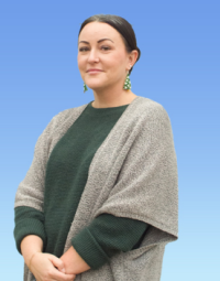 A profile shot of a woman with dark hair wearing green and white earrings, a dark green shirt and a grey cardigan.