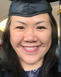 A graduate wearing a black gown, hat and tassel smiles broadly.