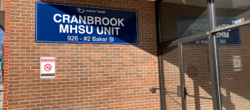 Brick building and glass doors, with blue sign on brick wall reading "Cranbrook MHSU Unit"