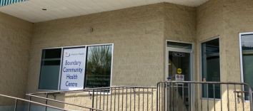 A yellow stucco building with a railing and ramp and a sign that says Boundary Community Health Centre