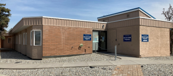 An orange brick building with a sidewalk and gravel in front and three signs that say Mental Health Programs