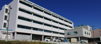 A large white five-storey building with dark windows and a white car parked in front with a blue sky in the background