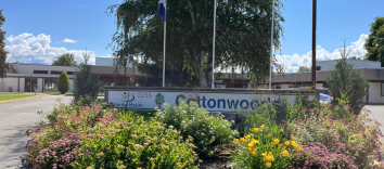 A long white sign reads Cottonwoods with flowers and shrubs in the foreground and a low white building in the background