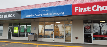 Buildings in a strip mall. There is a fully visible sign on one building with the Interior Health logo and the words Northills Centre Medical Imaging.