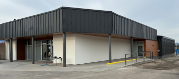 The exterior of a long building with a black roof and pillars and a white and brown wall.