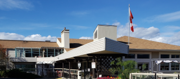 A low building with a brown roof, chimney, covered walkway and a Canadian flag.