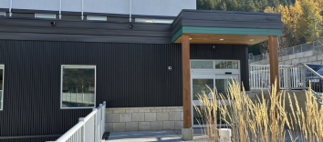 Nelson, BC mental health and substance use office. A black building with a covered front entrance set among trees and grasses.