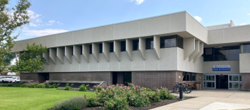 A long grey 2-storey building with green grass and low bushes in front.