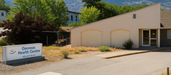 A slanted peach coloured building surrounded by trees. The sign in front says Osoyoos Health Centre.
