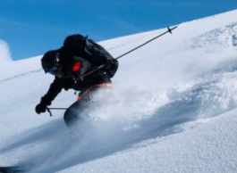 Man skiing down a hill wearing a helmet and backpack.