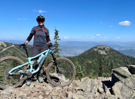 A woman poses for a picture with her mountain bike on a trail.