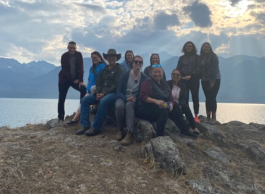 A group of people pose on a hill overlooking the water and mountains.