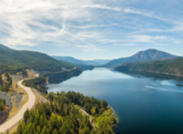A blue sky with hazy clouds above green mountains and a lake next to a winding highway