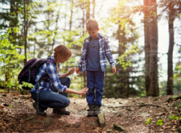 A child stands in the forest as an adult applies spray product on their jeans.