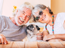 older couple smiles at the camera as they pet their dog