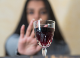 A blurred woman with long dark hair holds out her hand in front of her in front of a glass of wine