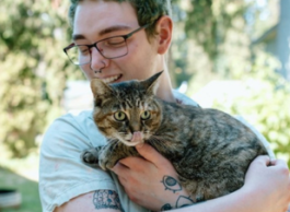 Young adult holding their cat, looking down at them with admiration.