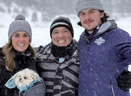 Three people: smiling woman with long brown hair, grey wool hat, man with grey and black striped jacket and striped toque, and tall man with brown hair, moustache, blue ski jacket and grey hat