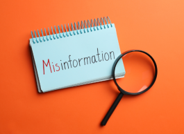 A magnifying glass sits on a spiral notepad with the word Misinformation in red and black against an orange background.