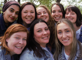 Group of eight people smiling at the camera in a park setting.
