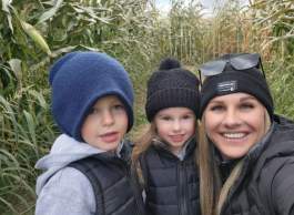 Woman wearing a black toque and sunglasses on her head posing with a young girl wearing a black toque and black puffy jacket, and a boy wearing a grey hoodie with a blue toque. 