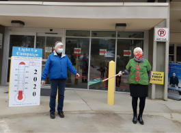 two seniors outside of Castlegar and District Community Health Centre showing fundraising efforts with signs while masked. 