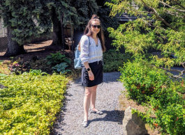 a brunette woman wearing sunglasses smiles at camera while walking on a path in a garden