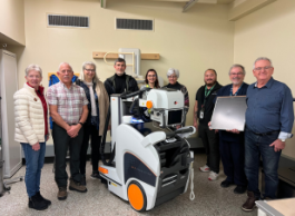 Group of eight individuals standing beside a new medical imaging machine in a hospital room.