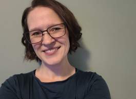 Head shot of smiling person with short brown hair wearing black frame glasses.