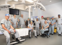 A cheerful group of people in scrubs pose for a picture in an operating room surrounded by medical equipment.